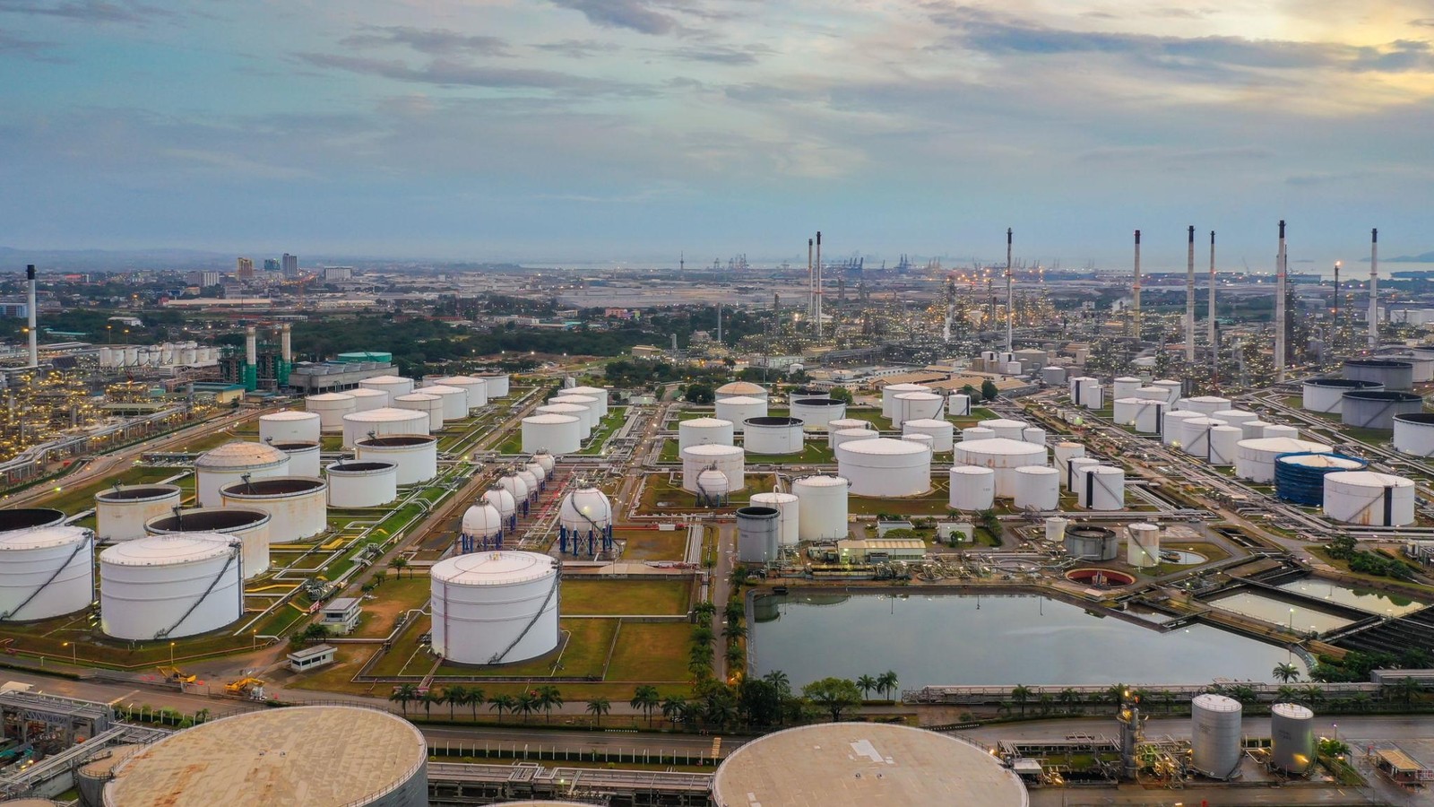Large oil storage tanks and refinery facilities near a coastal port at dusk